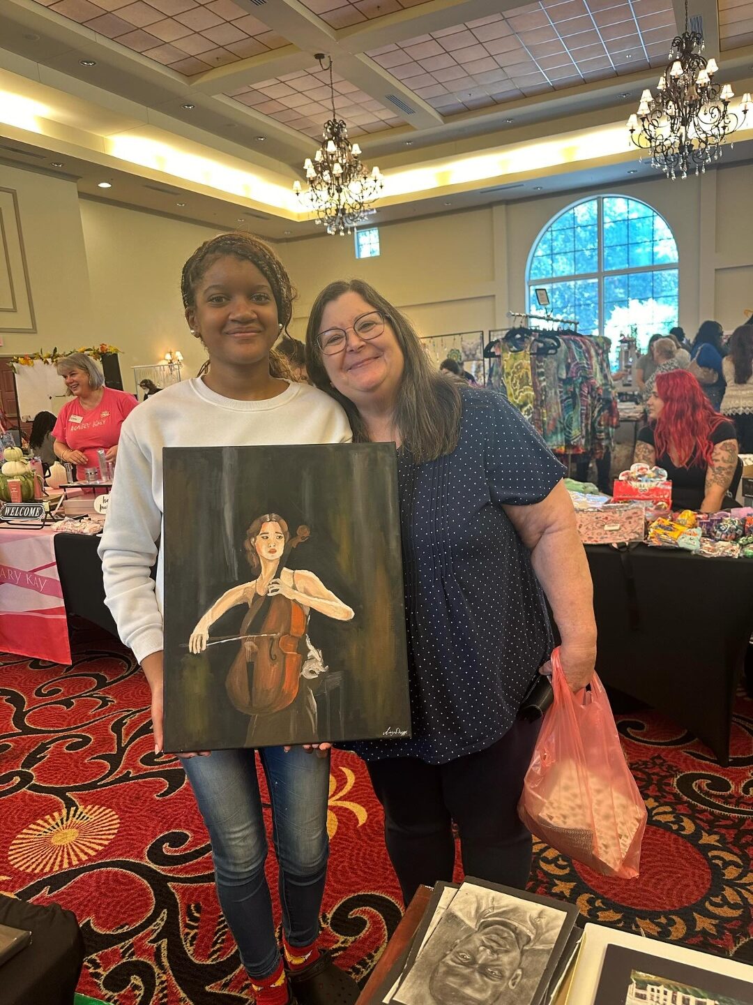 A woman holding the Cello painting alongside Aniya at an art market