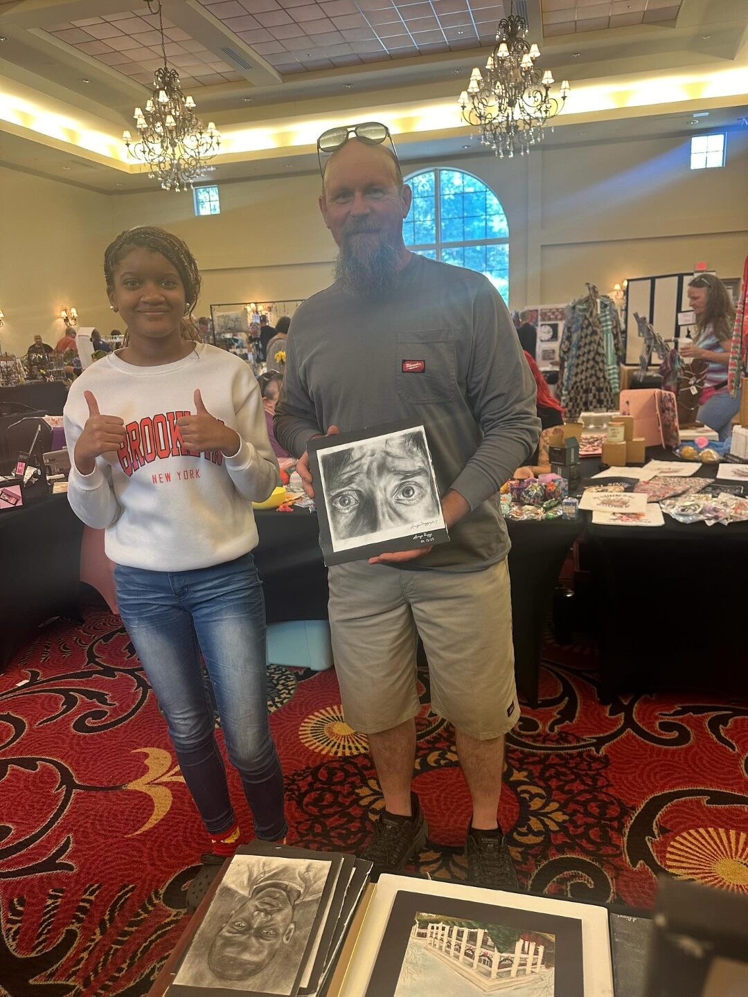 A collector holding a charcoal eye study drawing by Aniya, who gives a thumbs up
